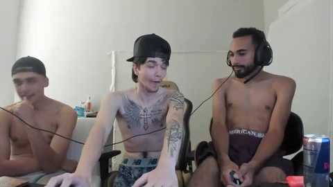 Media: Video of three shirtless, tattooed young men in casual clothes, sitting at a desk, playing video games, with a gaming headset on each.