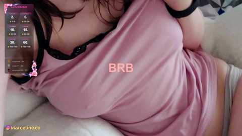 Media: Video of a woman in a pink tank top with \"BB\" on the chest, lying on a bed, with a digital clock showing 2:05 AM.