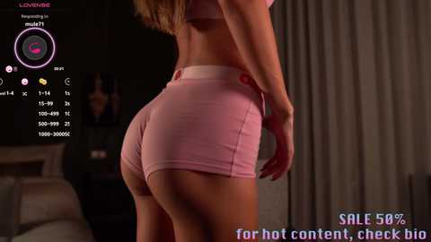 Media: Video of a slender woman in pink shorts and a matching sports bra, showcasing her toned buttocks. The background is a dimly lit bedroom with a bed and curtains. Text overlays offer a discount and mentions her username, \"Loveshawna.\