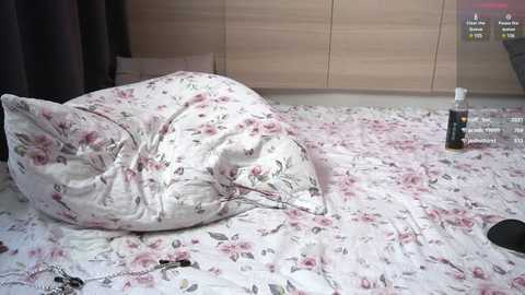 Media: Video of a bed with a floral-patterned white sheet and a pillow, a black spray bottle, and a remote control on a wooden-finish dresser in the background.