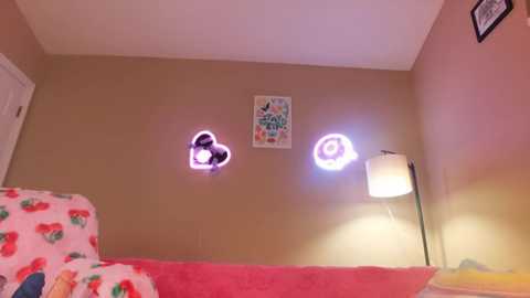 Media: Video of a child's bedroom with a pink blanket adorned with strawberries, beige walls, a white door, a framed picture, and a glowing pink and purple unicorn decal.