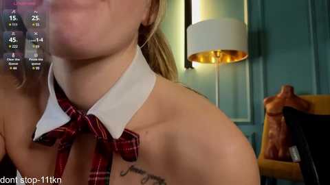 Media: A video of a blonde woman with a red plaid tie, partially naked, wearing a white collar, with a tattoo on her shoulder.