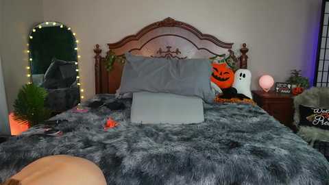 Media: A video of a cozy bedroom with a plush gray fur blanket, a carved wooden headboard, and Halloween-themed decor including a jack-o'-lantern, a ghost, and a lit mirror.