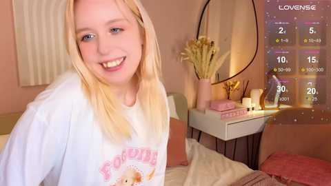 Media: A video of a smiling, blonde-haired young woman in a cozy bedroom with a round mirror, plants, and a calendar.