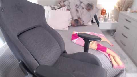 Media: Video of a gray gaming chair in a cluttered bedroom with a messy bed, pink and white-striped sheets, and a pink and yellow pillow.