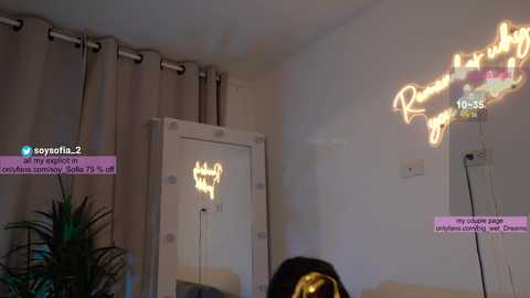 Media: Video of a cozy living room with beige curtains, a neon sign reading \"Ryoga,\" and a potted plant in the background. A person with a gold headband is visible in the foreground.