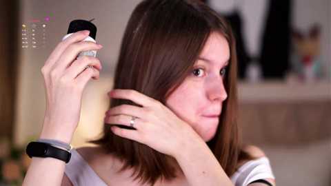 Media: Video of a young woman with light skin and brown hair, wearing a white off-shoulder top, applying hair gel with a black brush, and holding a silver ring.