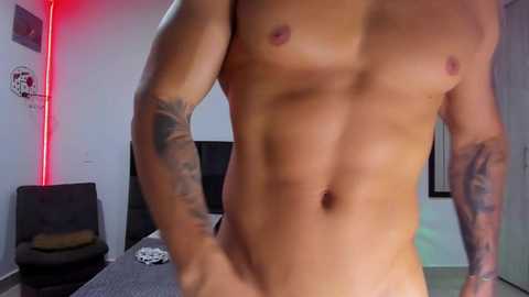 Media: Video of a fit, shirtless man with tanned skin, visible tattoos on arms, standing in a modern bedroom with minimalistic decor, red accent lighting, and a black chair.