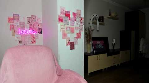 Media: A video showing a pink chair with a neon \"love\" sign, a collage wall, a TV, and minimalist shelves in a dimly lit living room.