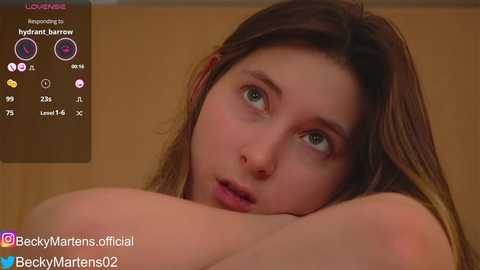 Media: Video of a young woman with fair skin and brown hair, lying on a bed, looking contemplative. Background is a plain beige wall.