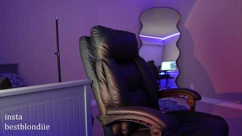 Media: Video of a cozy, dimly-lit home office with a plush, dark brown leather recliner chair facing a modern, purple-lit desk setup. The room has a minimalist, contemporary design with a large, curved mirror on the wall.