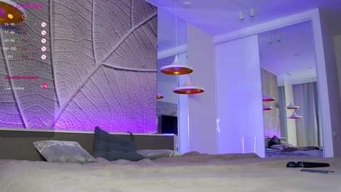 Media: Video of a modern bedroom with a gray leaf-patterned wall, purple lighting, beige bedding, and hanging red and white pendant lights.