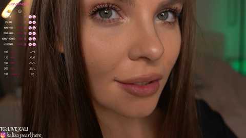 Media: A close-up video of a young Caucasian woman with fair skin, green eyes, and straight brown hair. She wears minimal makeup. The background is blurred, showing green and pink lighting. Text overlay with social media icons.