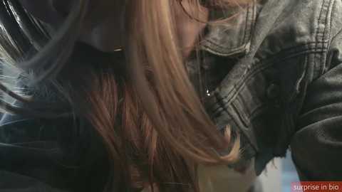 Media: Video of a young woman with long, straight blonde hair, wearing a gray leather jacket, caught in mid-motion, her head slightly turned to the right.