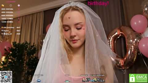 Media: Video of a blonde woman in a white veil, smiling, surrounded by pink balloons and a 'birthday' banner. The background includes a Christmas tree, suggesting a festive setting.