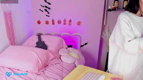 Media: A video of a pink-themed bedroom with a plush teddy bear, bat decals, and a guitar on the bed, lit with purple lights, featuring a person in a white robe in the background.