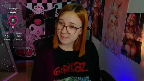 Media: A video of a young woman with shoulder-length orange hair, glasses, and a \"Gorillaz\" T-shirt, sitting in a room with vibrant posters and a video game interface.