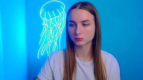 Media: Video of a young Caucasian woman with straight, long brown hair, wearing a white t-shirt, against a bright blue backdrop with a glowing, neon jellyfish illustration.