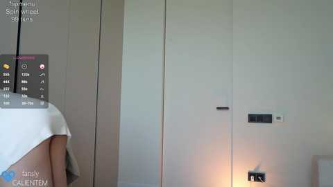 Media: Video of a minimalist bedroom with white walls, a bed covered in white sheets, and a small nightstand with a lamp. A digital thermometer and a temperature gauge are visible on the left.