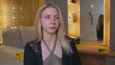 Media: Video of a young Caucasian woman with long blonde hair, wearing a black lace top and robe, standing in a modern bedroom with wooden accents, a bed, and a mirror.