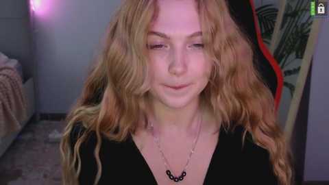 Media: Video of a young woman with long, wavy, light brown hair, fair skin, and a small black necklace, sitting in a dimly lit bedroom with a bed, red and black tapestry, and purple wall.