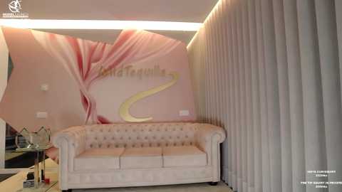 Media: Video of a modern waiting room with a beige tufted sofa, a large pink flower mural, and vertical blinds in the background.