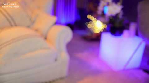 Media: Video of a plush, white armchair in a dimly lit room, with a blurred, glowing white light bulb and purple ambient lighting in the background. Text overlay reads, \"I hope you're having a good night.\