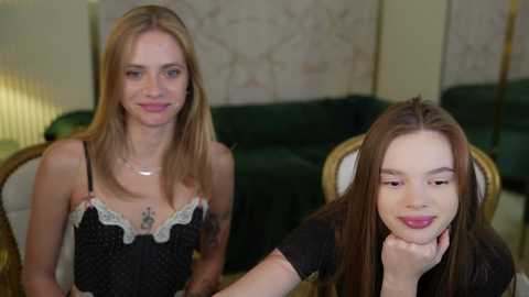 Media: Video of two young women in a cozy living room; one blonde in a black dress with lace, the other brunette in a black top, both smiling.