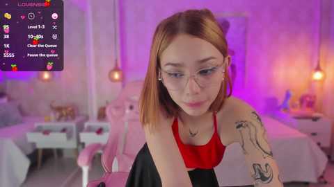 Media: A video of a fair-skinned woman with straight brown hair, wearing glasses, a red top, and tattoos, sitting in a pink chair, surrounded by a neon-lit, modern room with a digital overlay.