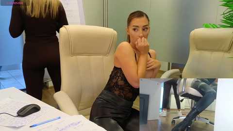 Media: Video of a woman with medium skin tone and long brown hair, wearing a black lace bodysuit, sitting in an office chair, covering her mouth, while a woman in black attire walks by.