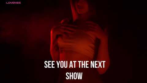 Media: Video of a woman with fair skin, dark hair, wearing a tight white top, standing in a dimly lit, red-lit room. Text reads, \"SEE YOU AT THE NEXT SHOW.\