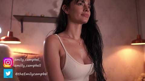 Media: Video of a young woman with long black hair, fair skin, wearing a beige tank top, standing indoors with warm lighting, social media icons visible.