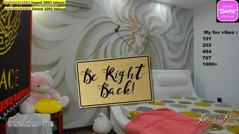 Media: A video of a modern bedroom with a large, wooden sign saying \"Be Right Back!\" hanging from the ceiling. The room features a bed with a white duvet and green polka dot sheets, a pink teddy bear, and a vibrant mural of a dragon.