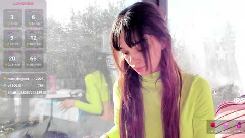 Media: Video of a young woman with long, straight brown hair in a bright yellow top, looking down with a thoughtful expression. Background shows a city street with blurred people and buildings.