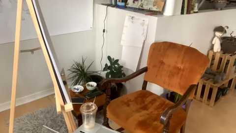 Media: Video of a cozy, cluttered room with a brown armchair, a wooden easel, a white board, and a stuffed toy on a shelf.