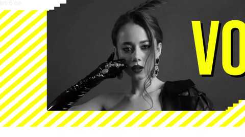 Media: Black-and-white video of a woman with a bold, asymmetrical hairstyle, wearing a black, shiny, textured glove and a high-neck, structured top. Background features a yellow, diagonal striped pattern with the word \"VOGUE\" partially visible.