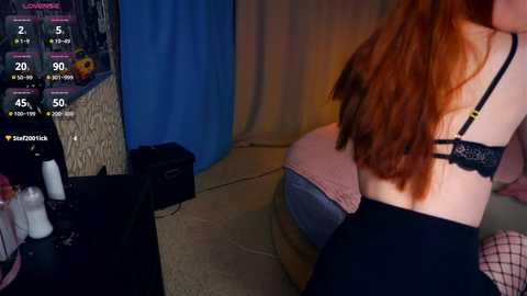 Media: Video of a woman with long red hair, wearing black lingerie, sitting on a bed. Background shows a blue curtain, a clock displaying 4:50, and a \"Scootie\" logo.