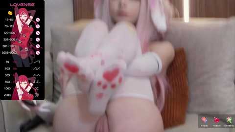 Media: A blurry video of a young woman with pink hair and bunny ears, wearing white lingerie, sitting on a couch.