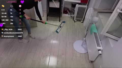 Media: A video captures a man vacuuming a wooden-floored apartment with a white radiator and a window in the background. The image has a live-stream overlay with hearts and usernames.