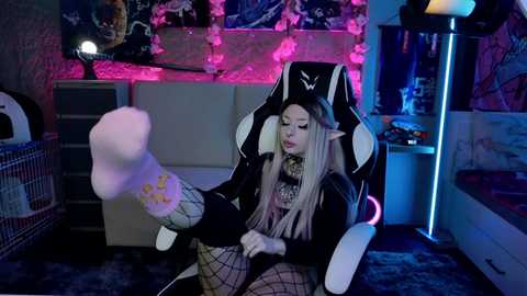 Media: Video of a young woman in a gaming chair, wearing a black and white outfit, with long blonde hair, playing with a soft, fluffy toy.