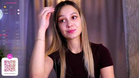 Media: Video of a young Asian woman with long, straight, ombre hair, wearing a black top, smiling while touching her hair. Background features a blurred, modern indoor setting with a QR code on the left.