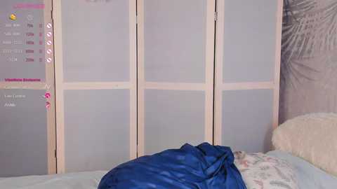 Media: Video of a cozy bedroom with light-colored wooden room divider, a blue blanket, and a floral pillow.