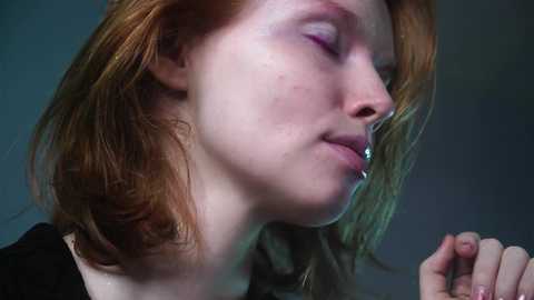 Media: A close-up video of a young, pale-skinned woman with long, red hair, wearing a nose ring, and looking contemplative, with a blurred background.