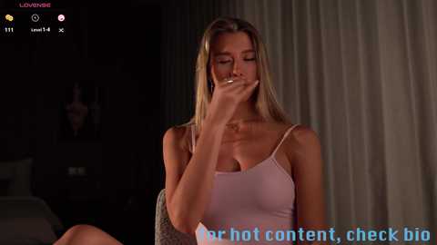 Media: Video of a blonde woman in a light pink tank top, covering her mouth with her hand, in a dimly lit room with a \"check big\" watermark.