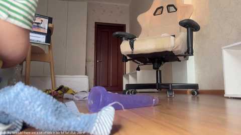 Media: Video of a messy bedroom with a child's plush toy, scattered toys, and a gaming chair; wooden floor, beige walls, and a partially open door.