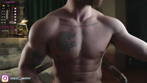 Media: Video of a shirtless, muscular man with a tattoo across his chest and biceps, sitting indoors, surrounded by gaming-related virtual overlays.