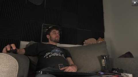 Media: Video of a man in a black t-shirt, lounging on a beige couch, holding a controller, with a cat sleeping behind him.