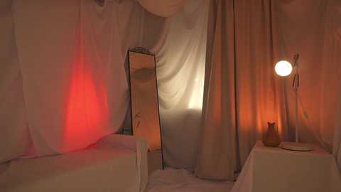 Media: Video of a dimly lit, minimalist bedroom with white drapes, a tall mirror, and a round lamp casting warm, orange light. The scene exudes a serene, intimate atmosphere.