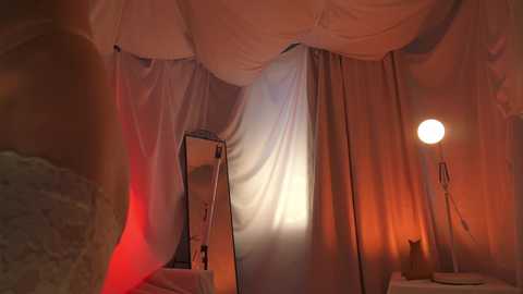 Media: A video of a cozy, dimly lit bedroom with beige curtains, a small white table lamp, and a mirror reflecting light. The room exudes a warm, intimate atmosphere.