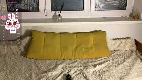 Media: Video of a cozy bedroom with a plush white bedspread and a mustard-yellow pillow. A white window frame with frosted glass and a black window cleaner on the sill is visible.